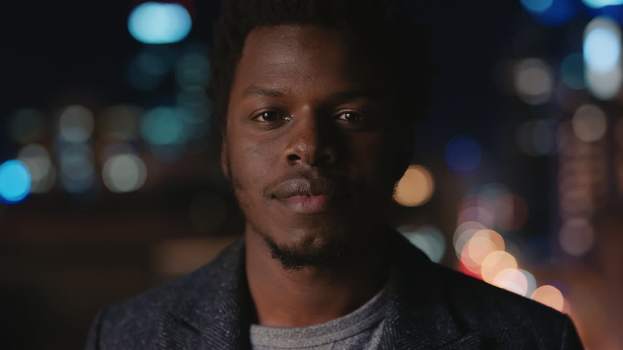 portrait of attractive young african american man on rooftop at night with bokeh city lights in urban skyline background