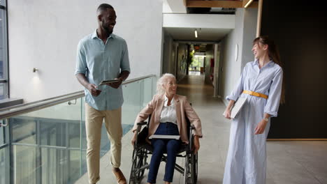 walking in office, diverse colleagues one using wheelchair discussing work with woman in wheelchair