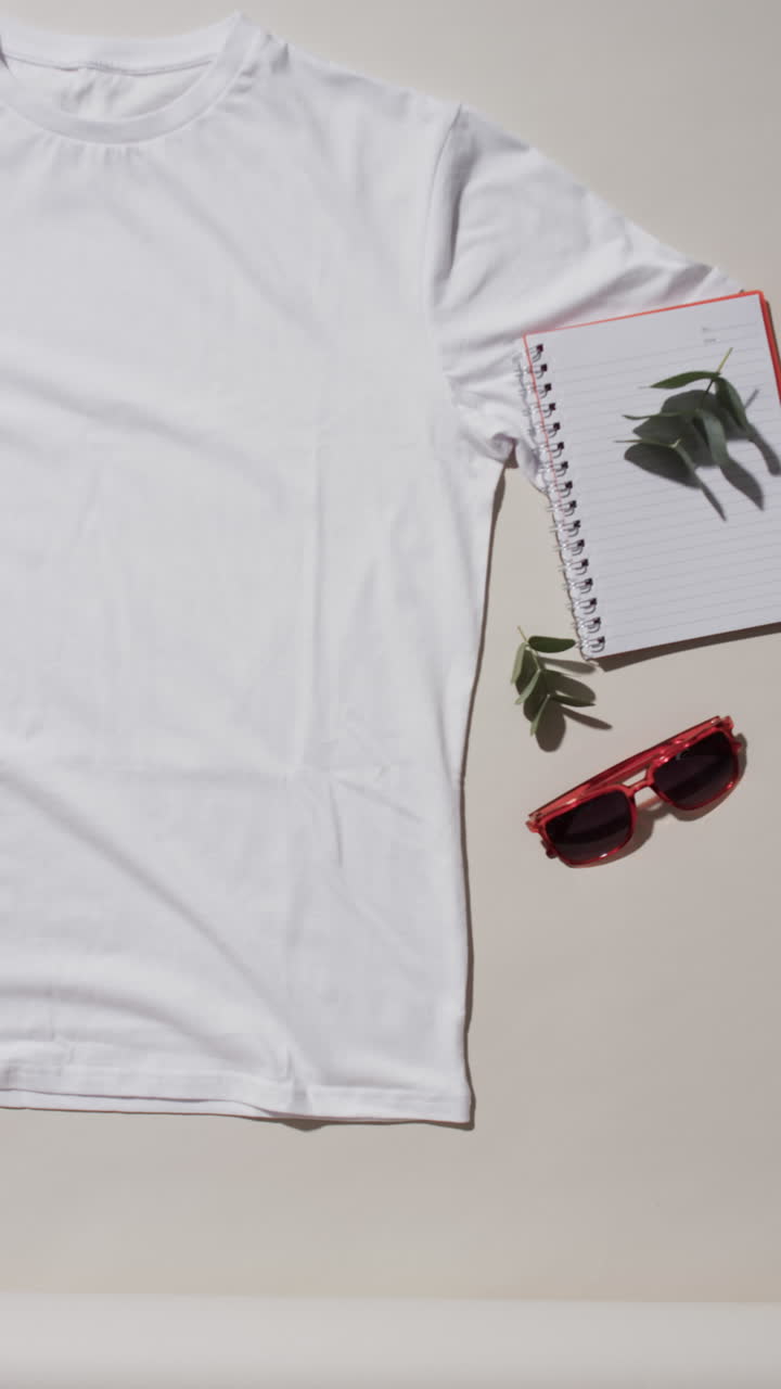 Video of orange t shirt, notebook, sunglasses and copy space on white background