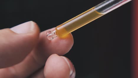 man holds pipette with brown liquid on black background