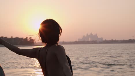 Nahöstliches-Modell-In-Sexy-Kleid-Mit-Schal,-Der-Im-Wind-Fliegt,-Posiert-Mit-Atlantis-Hotel-Und-Meer-Im-Hintergrund-Bei-Sonnenuntergang-In-Dubai