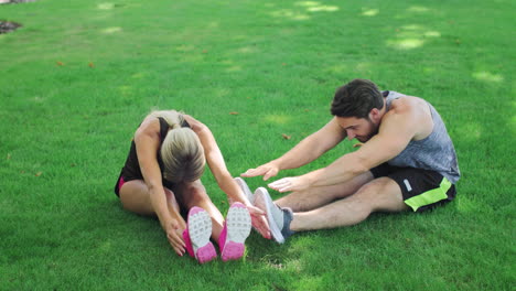 pareja joven estirando antes del entrenamiento de fitness en la hierba verde en el parque de verano