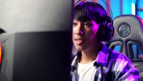 close up of excited asian teen boy gamer playing video game on computer
