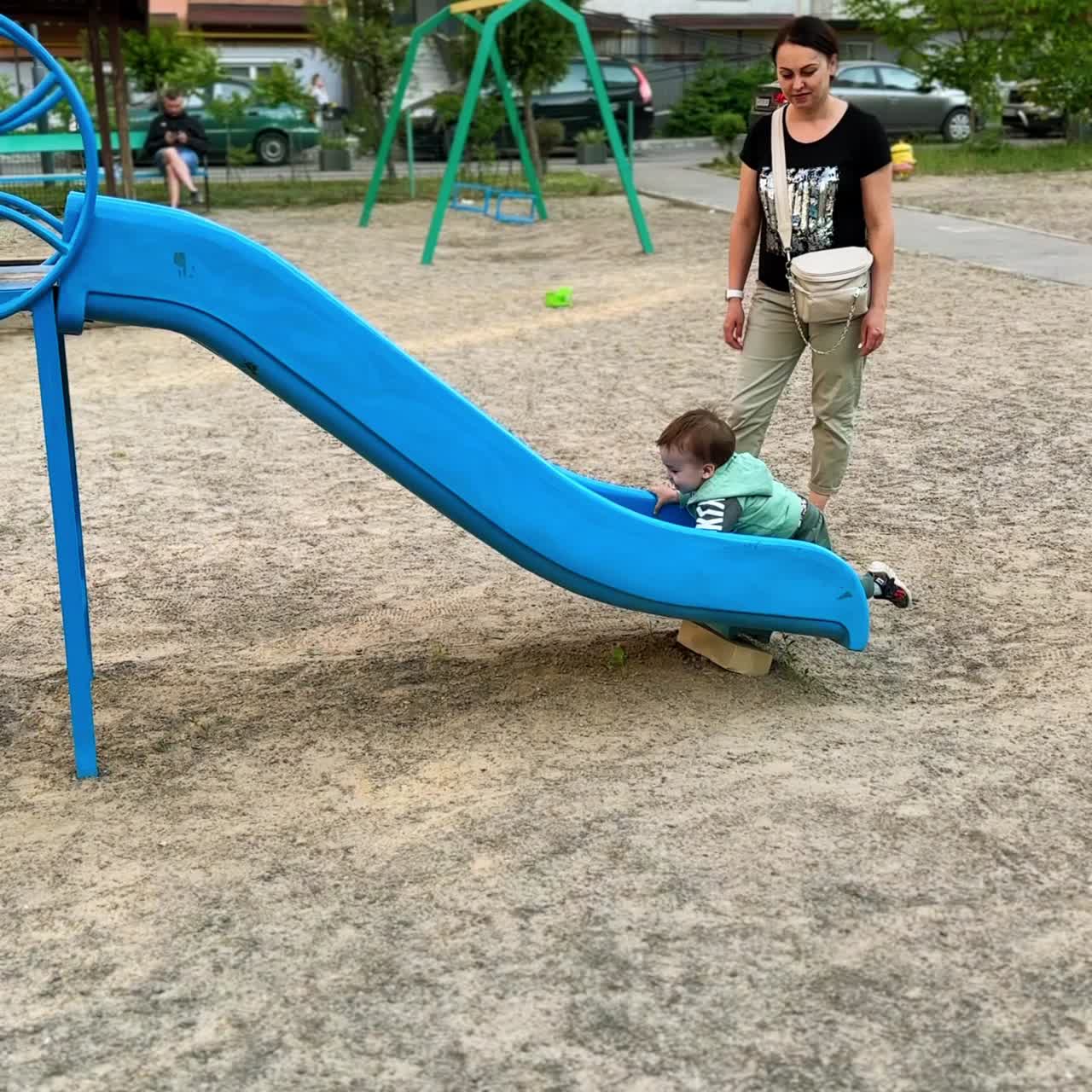 Little kid tries to climb on the slide from below. Baby boy changes his mind and runs to the stairs followed by mom. Vertical screen