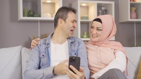 Muslim-family-laughing,-looking-at-the-phone-and-having-fun.