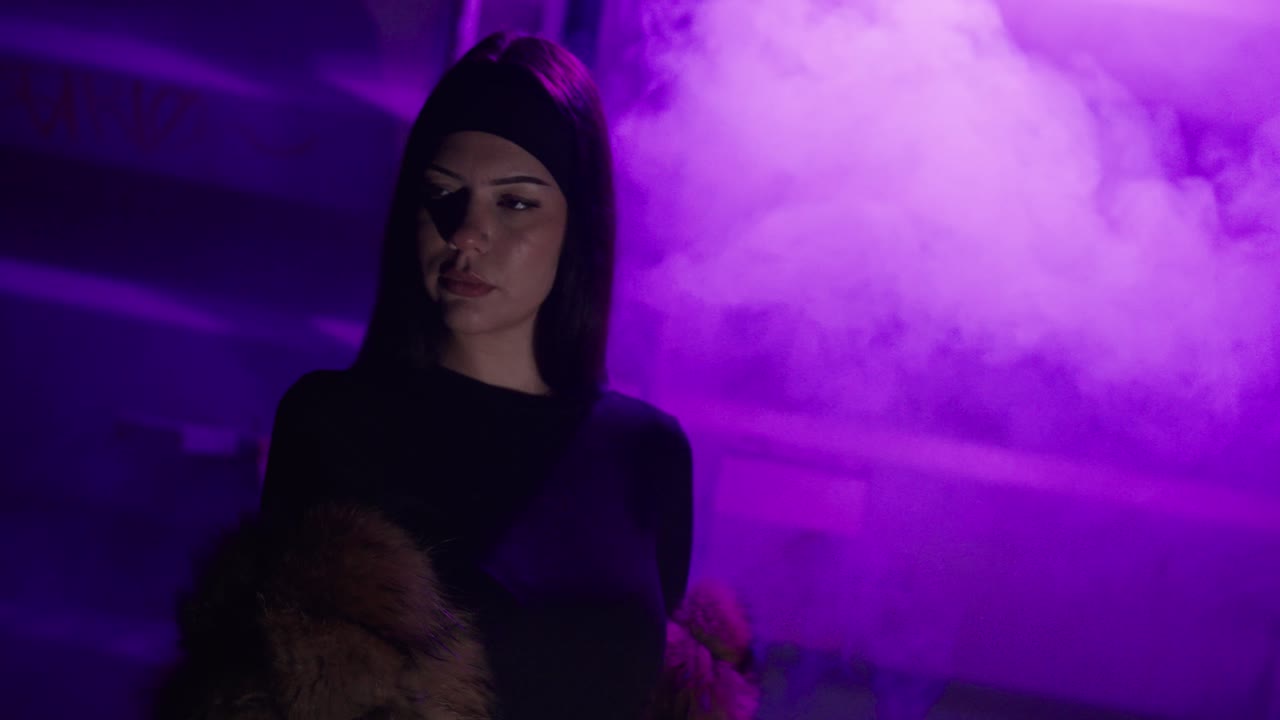 Una donna in piedi di fronte a uno sfondo viola illuminato al neon e pieno di nebbia fluttuante, che crea un’atmosfera urbana cinematografica, misteriosa e suggestiva