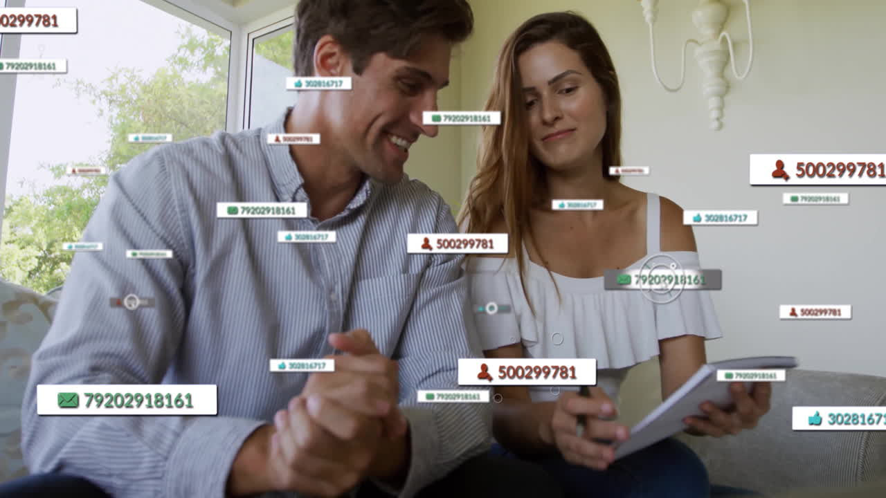 Man and woman reviewing social media metrics on sofa, showing floating numeric IDs, thumbs-up icons