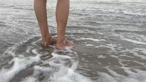 Wellen-Schlagen-Auf-Die-Beine-Eines-Indischen-Mädchens,-Das-Mit-Fußkettchen-Am-Ufer-Steht
