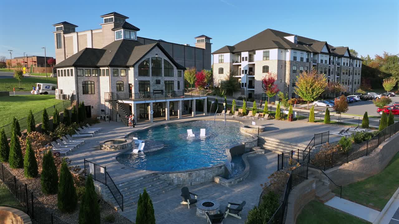 Aerial approaching shot of community swimming pool in luxury apartment neighborhood. Sunset time in american suburb district.Colorful trees in autumn season. Noble expensive houses in USA.