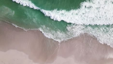 Still-drone-shot-over-beach-with-waves-crashing-onto-the-white-beach-sand
