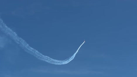 a skilled pilot performs a thrilling acrobatic loop and dive maneuver in a stunt plane, leaving a long white smoke trail across the clear blue sky during an airshow