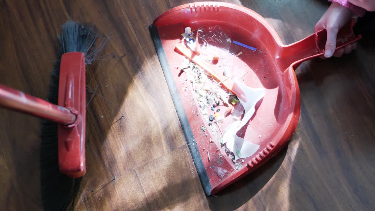 barrer el piso de madera marrón sucio en una bandeja para el polvo con una escoba roja y un niño ayudando a sostenerlo durante el bloqueo pandémico covid arriba hacia abajo clip de ángulo pov - en el cine 4k