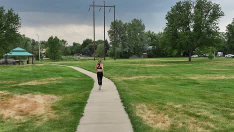 fit and healthy practices. a woman does cardio while running on a stormy day through a city park