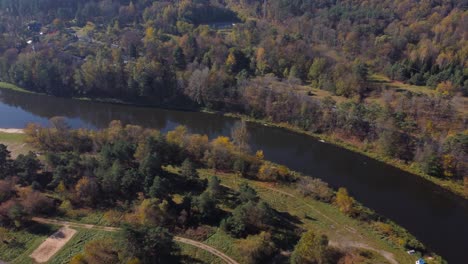 AERIAL-Side-Panning-Shot-of-a-River-and-a-River-Beach-Surrounded-by-Autumnal-Forests-in-Vilnius,-Lithuania