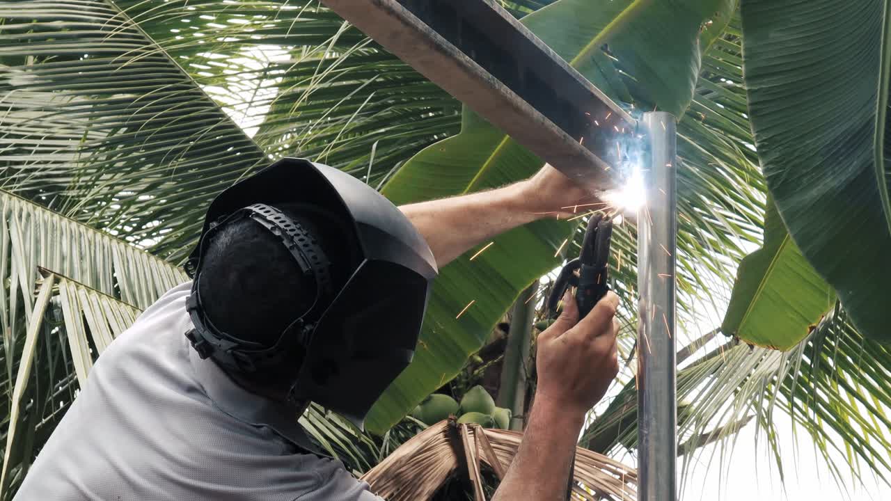 soldador profesional que emplea una máquina de soldadura industrial para unir dos piezas de metal creando una estructura metálica como parte de su trabajo diario en una pequeña empresa local