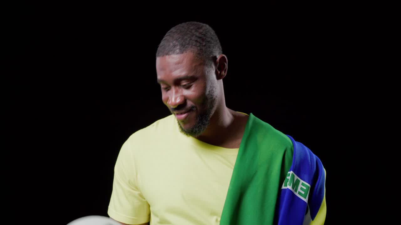 Uomo afroamericano che tiene un pallone da calcio in studio, in equilibrio e sorridendo, esprimendo orgoglio con una bandiera.