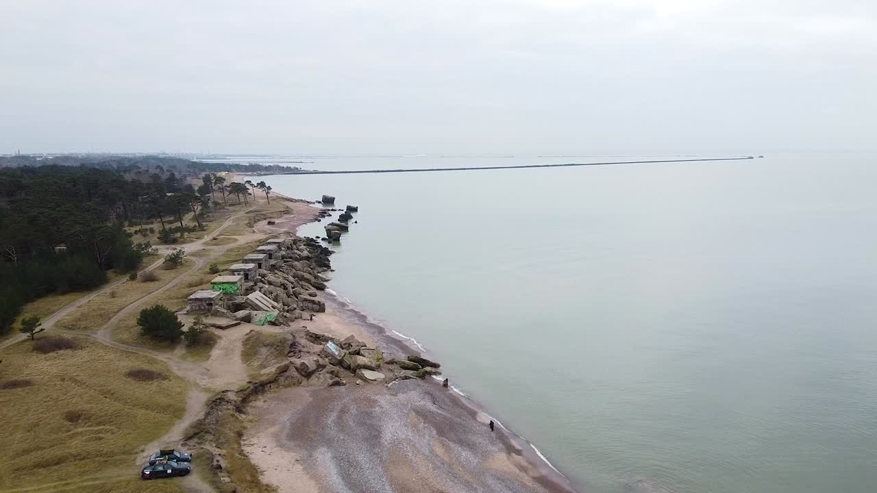 Ilmakuva hylätystä rannikkolinnoitusrakennuksesta Karostan pohjoislinnoituksilla Itämeren rannalla Liepajassa pilvisenä kevätpäivänä, laaja eteenpäin liikkuva dronekuva