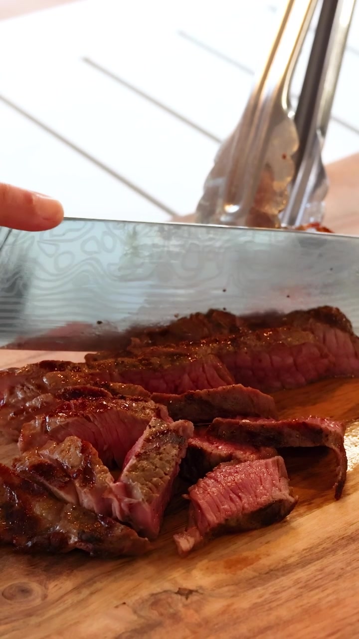 Un cuchillo corta un bistec de res cocido sobre una tabla de madera, resaltando la carne jugosa y tierna con luz natural.