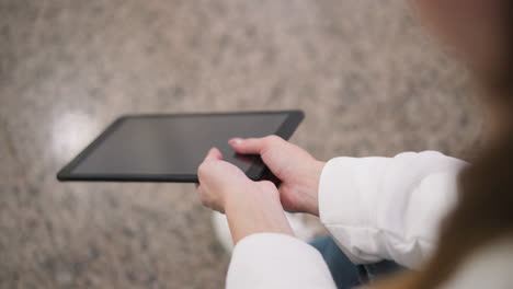 close up of hands in white sleeve gently holding tablet while seated on granite floor, hands sway tablet slightly, creating subtle reflections on screen