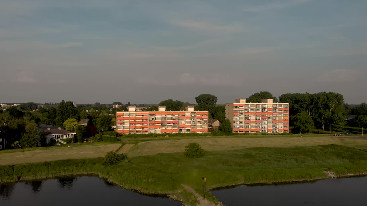 네덜란드 주트펜(zutphen)의 네덜란드 범람원 풍경을 드러내는 천천히 뒤로 움직이는 이셀(ijssel) 강을 따라 폐쇄된 오렌지 차양이 있는 고층 아파트 건물의 공중 접근
