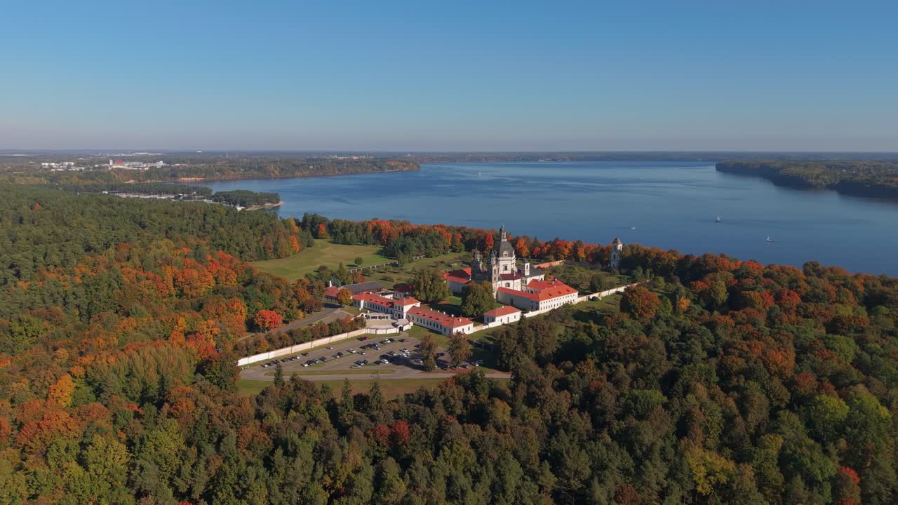 Aerial view of Pažaislis Monastery in Kaunas, Lithuania, surrounded by colorful autumn forest and Kaunas Reservoir in the background. A scenic and historic Baroque religious landmark