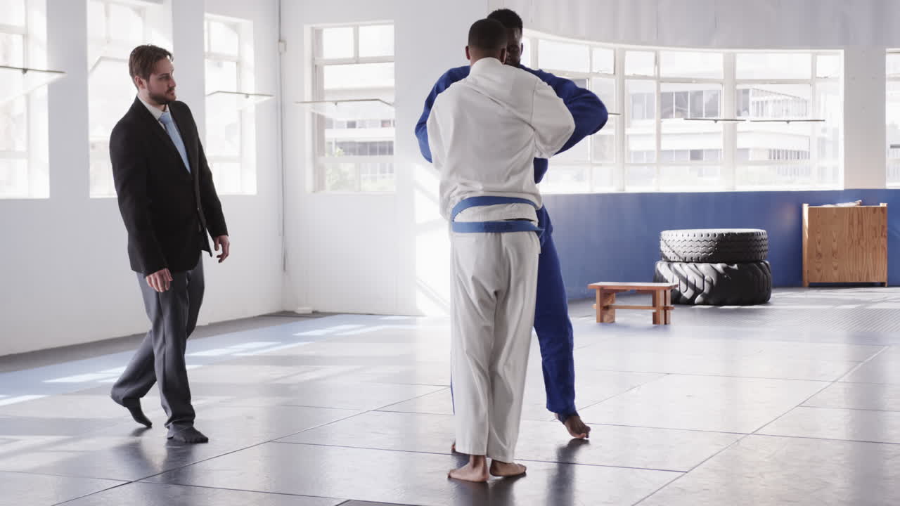 Judo practitioners sparring in dojo while instructor observes their technique