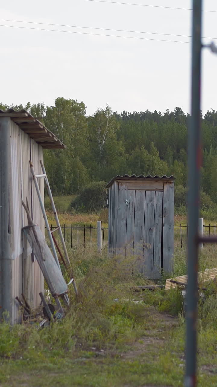 Barn with open door boards pile and outdoor handmade toilet in summerhouse yard. Small houses and construction materials in village. Countryside life