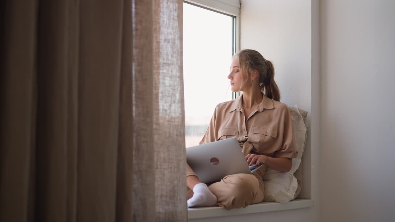 Donna segue corsi di formazione a distanza tramite laptop, seduta vicino alla finestra.