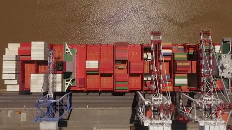 cargo ship loaded with colorful containers docked at a busy port, aerial view