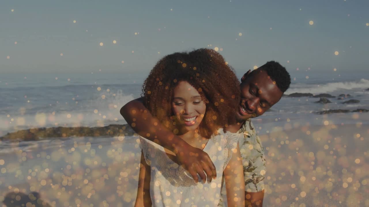 Beach couple beaming under bokeh with man stepping in looping arms around woman in travel marketing
