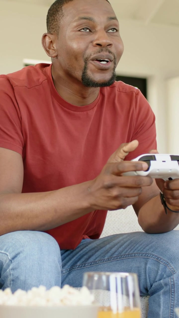 Vertical video: Reacting to game man pressing white pad on couch, red tee, popcorn and orange drink