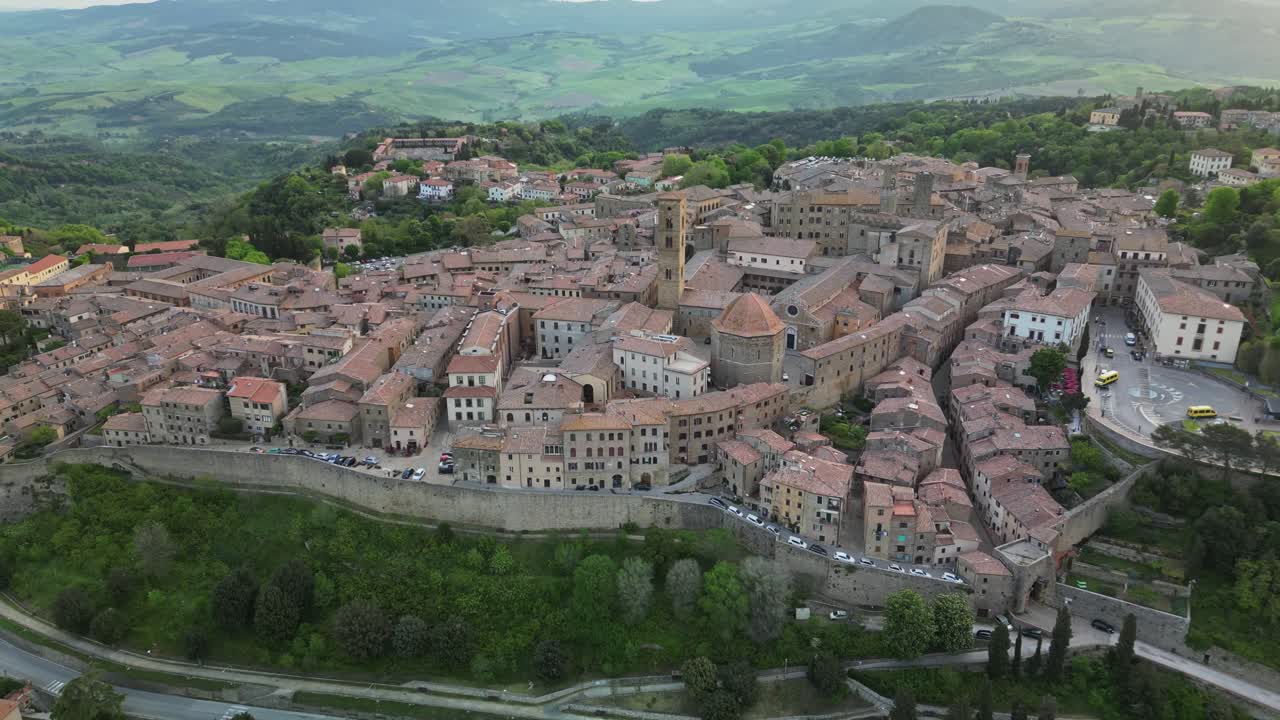 Vista drone di Volterra con mura cittadine medievali, edifici storici e le dolci colline toscane che circondano il centro storico in Italia.