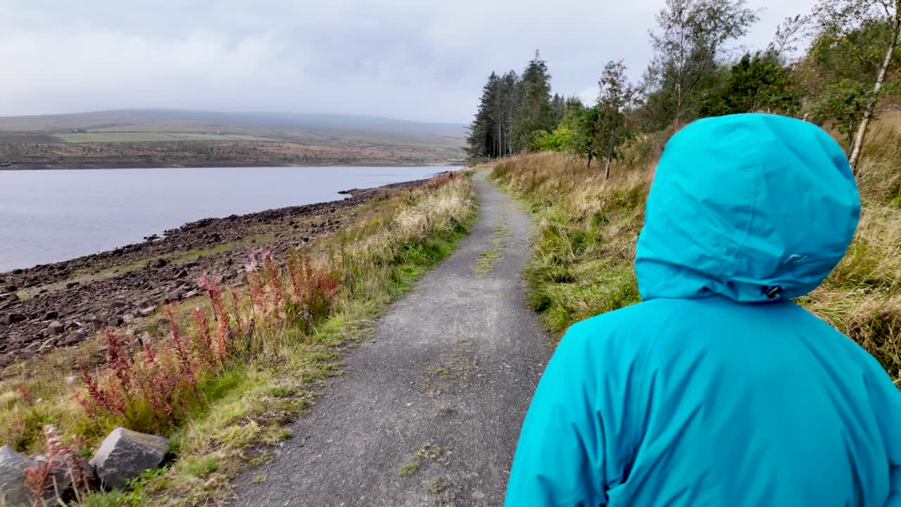 Person in blue rain jacket walking white dog beside Burnhope Reservoir