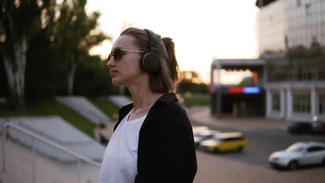 trendy, attractive girl in stylish youth clothes freely dancing outside on the street. listening to the music in black