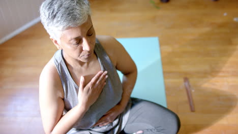 una mujer de dos razas está meditando en una alfombra de yoga en casa.