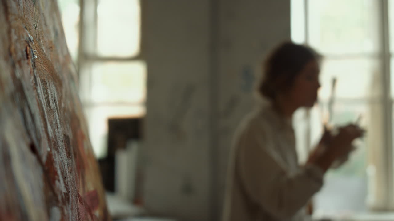 숙련된 화가가 스튜디오에서 아침을 보내고 있습니다. 소녀는 흐릿한 배경에서  ⁇ 고 있습니다.