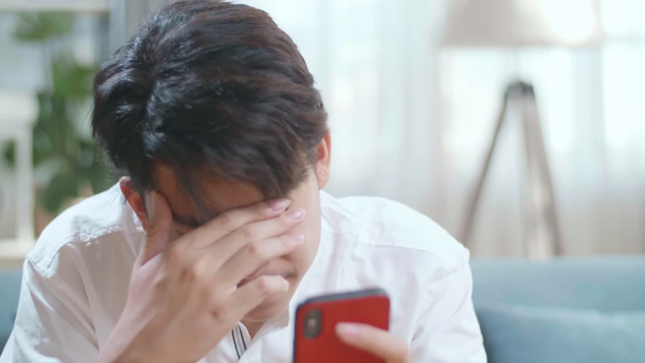 Close Up Of Asian Man Being Tired While Using Smartphone In The Living Room