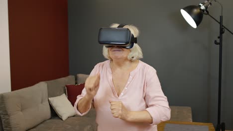 Happy-senior-woman-in-virtual-reality-headset-glasses,-trying-to-touch-something,-watching-3D-video