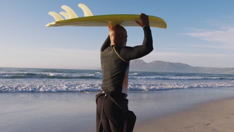 älterer afrikanisch-amerikanischer mann mit einem surfbrett auf dem kopf am strand