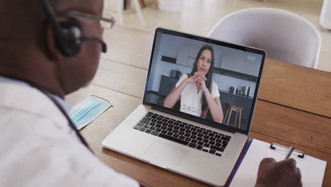 hombre de negocios afroamericano sentado en un escritorio usando una computadora portátil haciendo una videollamada con una colega