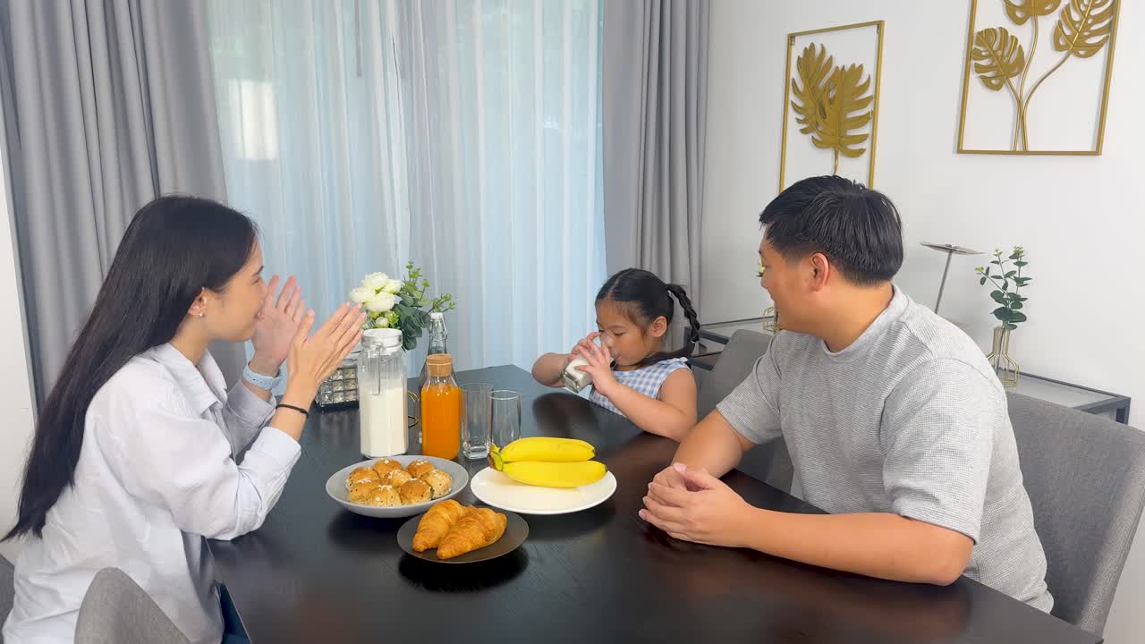 A family of three enjoys breakfast together at a dining table, sharing food and conversation in a bright, cozy setting