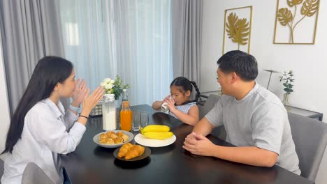 a family of three enjoys breakfast together at a dining table, sharing food and conversation in a bright, cozy setting