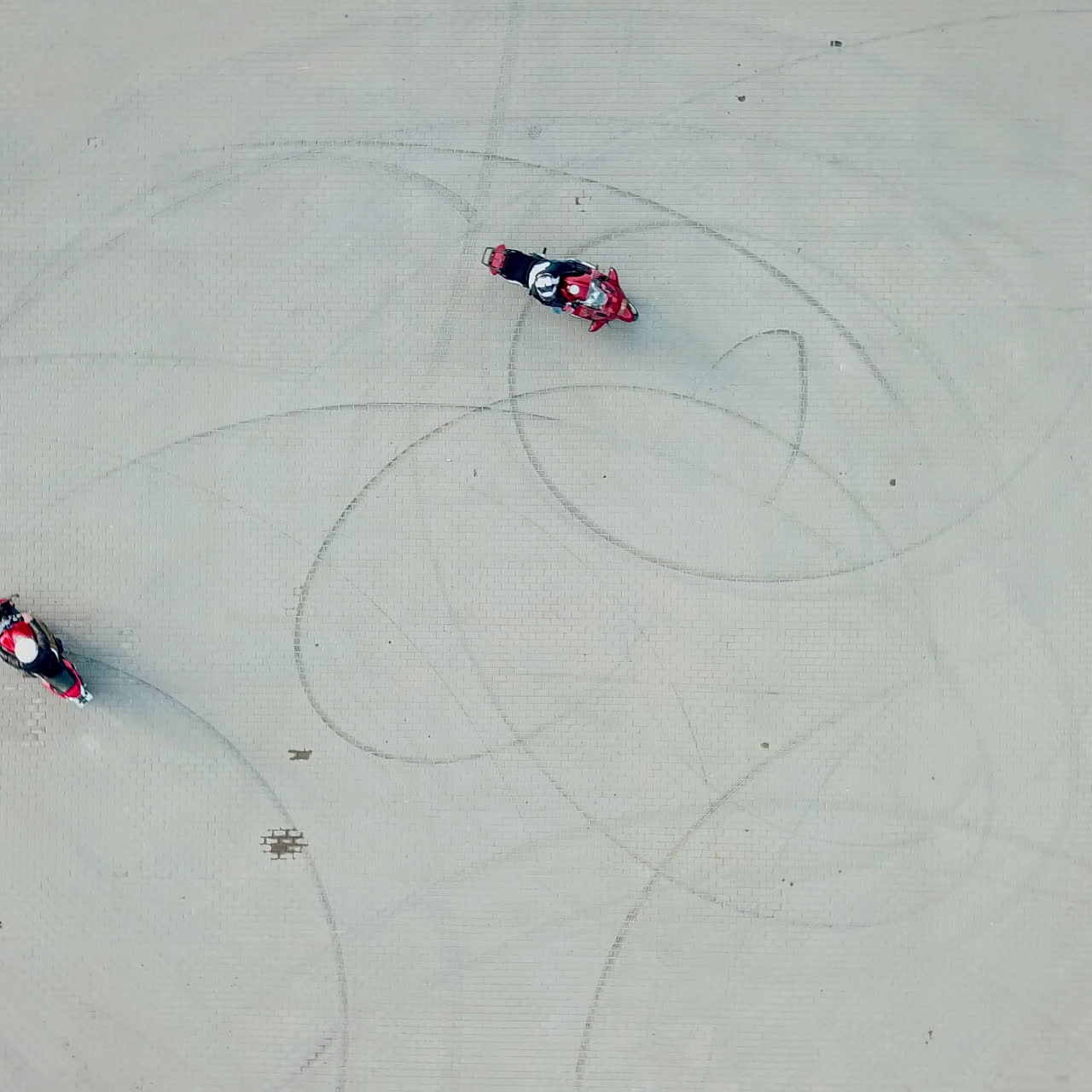 Aerial view of two red motorbikes racing high speed on a road in a circle way. Drivers on their motorcycles training on a race track outdoors. Camera moves around in a circle.