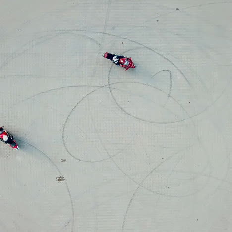 aerial view of two red motorbikes racing high speed on a road in a circle way. drivers on their motorcycles training on a race track outdoors. camera moves around in a circle.