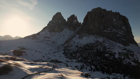 Aerial-View-of-Sella-Pass-on-Sunny-Spring-Day,-Winding-Road-in-Snow-Capped-Hills-of-Italian-Dolomites