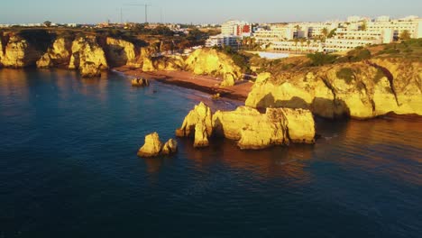 puesta de sol de la hora dorada golpeando el acantilado de piedra mientras el dron se acerca a una hermosa playa