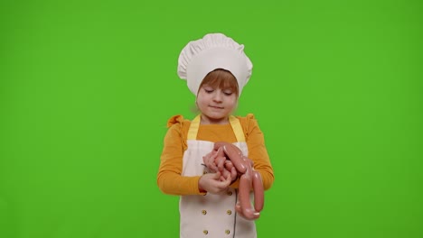 child girl dressed in apron like chef cook sniffing sausages, recomending and showing them to camera