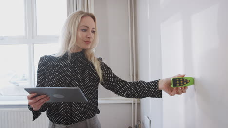 female realtor with digital tablet measuring room with laser measure