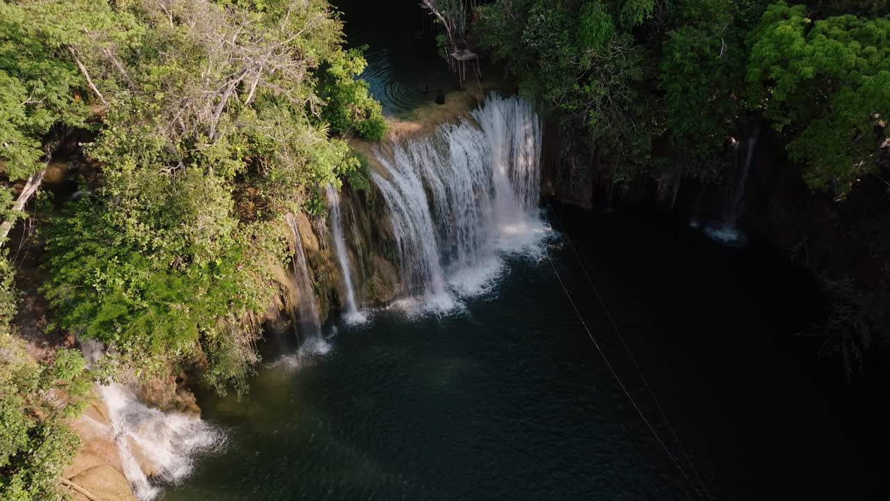 wide aerial of waterfalls plunging into a dark jungle pool surrounded by lush rainforest in Petén, Guatemala.