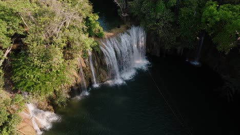 wide aerial of waterfalls plunging into a dark jungle pool surrounded by lush rainforest in petén, guatemala.